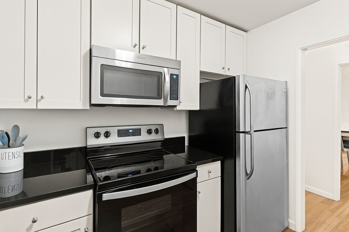 A modern kitchen with white cabinets, a stainless steel microwave, a black stove, and a refrigerator.