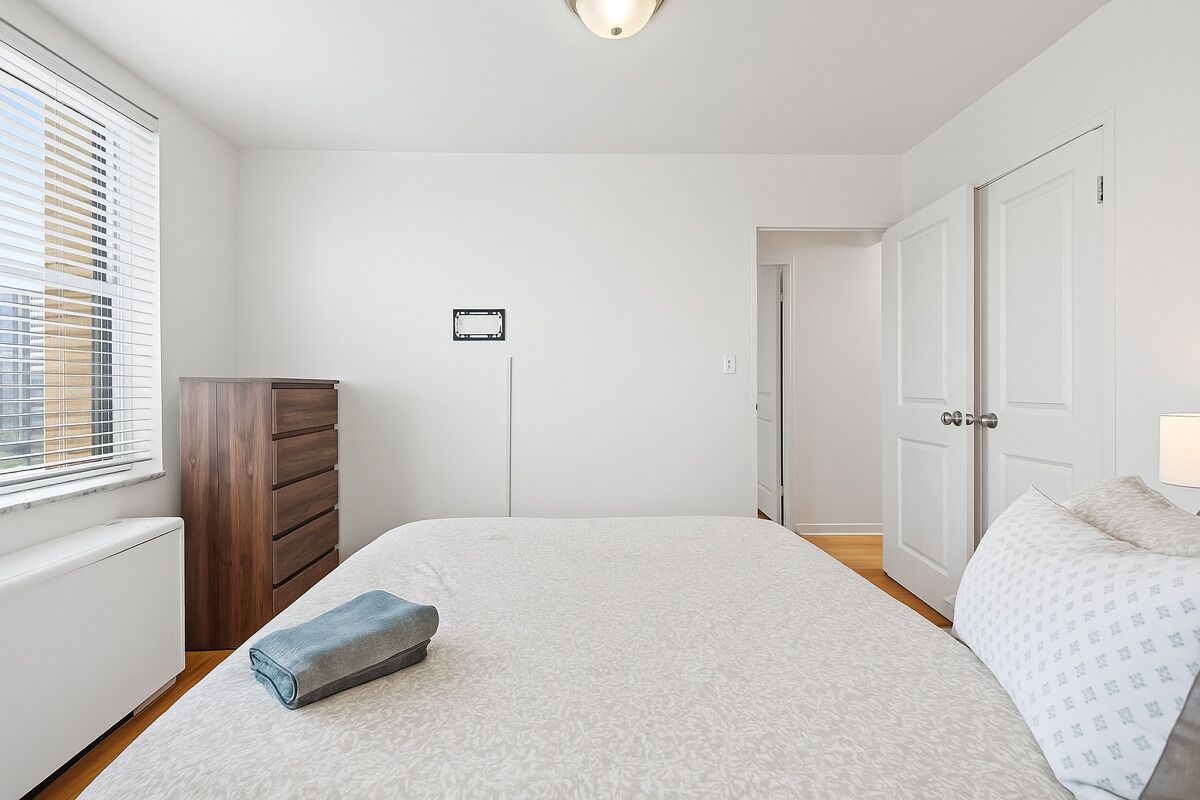 A bedroom with a large bed, a wooden dresser, a radiator, and a door leading to another room.