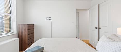 A bedroom with a large bed, a wooden dresser, a radiator, and a door leading to another room.