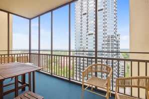 Un balcon avec une table et des chaises, d’où l’on peut admirer un immeuble de grande hauteur et une vue lointaine.
