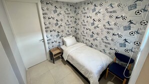 Een slaapkamer met een bed, een stoel, een klein houten krukje en een muur met fotobehang met voetbalthema.