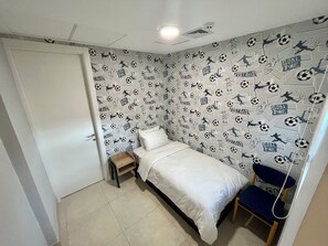 Ein Schlafzimmer mit einem Bett, einem Sessel, einem kleinen Holzhocker und einer Wand mit Fußball-Tapete.