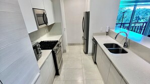 Een moderne keuken met witte kastjes, roestvrijstalen apparatuur en een groot raam met uitzicht.