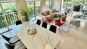 Een ruime eethoek met een marmeren tafel, zwarte stoelen en een groot raam met uitzicht op een balkon met planten.
