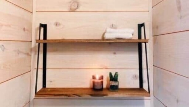 A wooden interior with two shelves, one with a white towel and the other with a candle and a small plant. - The Oculus Tinyhouse (Triadelphia)