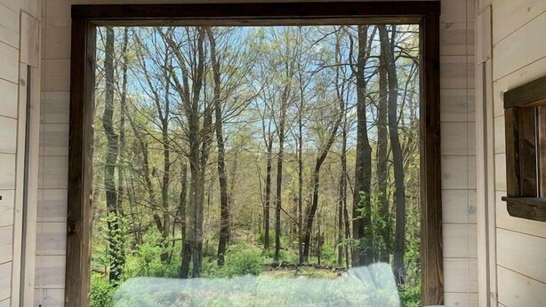 A room with a large window providing a view of a forest.
