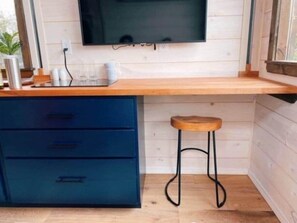 Eine Küche mit einer Holzausziehtheke, einem blauen Schrank, einem Hocker und einem an der Wand befestigten Fernseher.