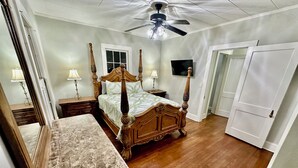 Une chambre à coucher avec un lit à baldaquin, un ventilateur de plafond, un grand miroir et un téléviseur fixé au mur.