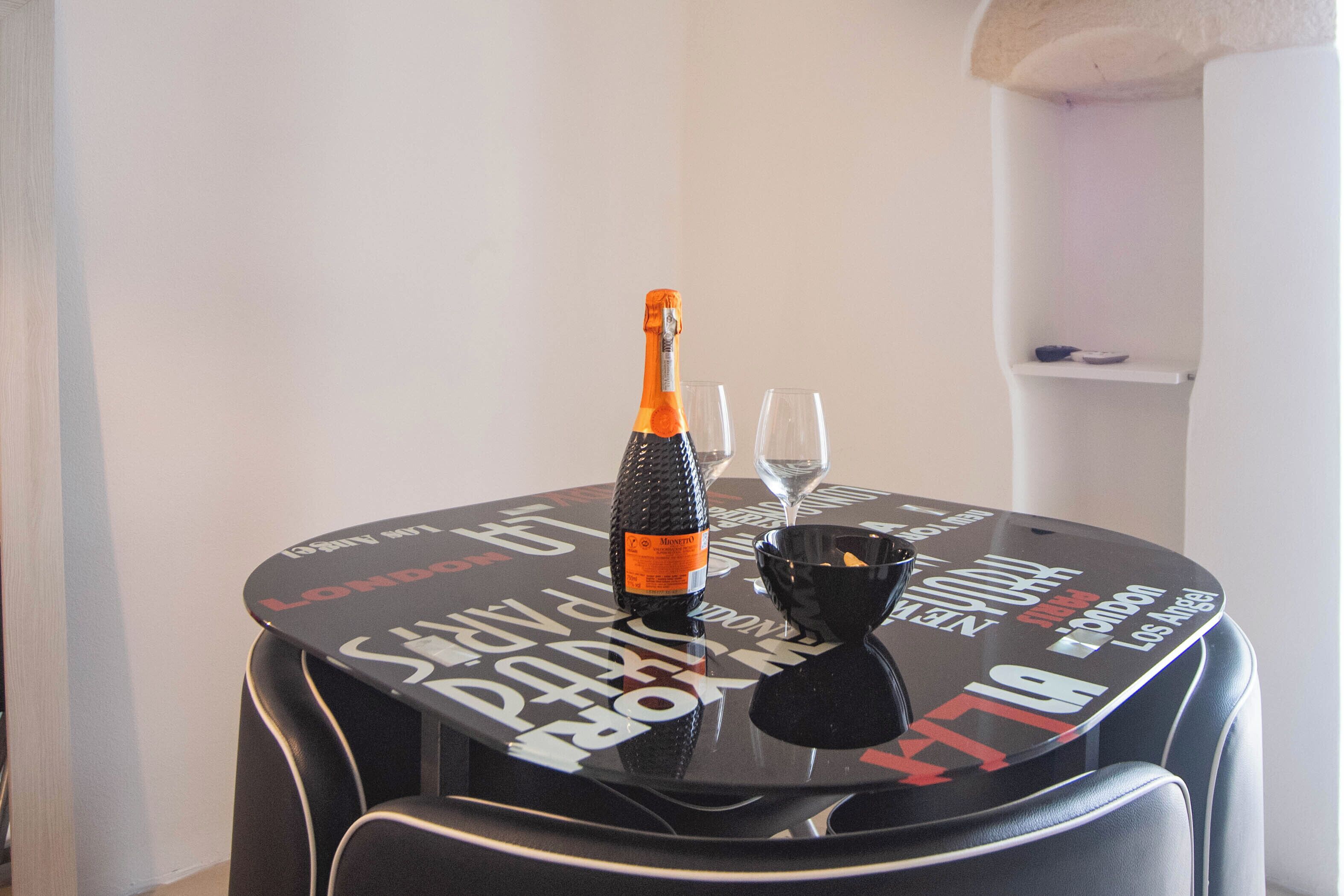 Et rundt bord med champagne, to glas og en lille skål.