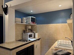A compact kitchen with a microwave, coffee maker, and kettle on the countertop, a dish rack, and a small sink.