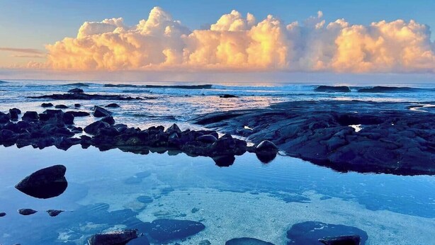 Eine felsige Küste mit ruhigem Wasser, das Himmel und Wolken spiegelt.