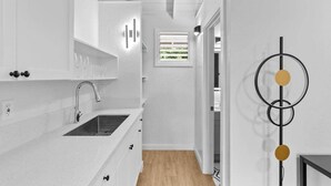 Eine moderne Küche mit weißen Schränken, einer Spüle und einem Fenster mit Jalousien.