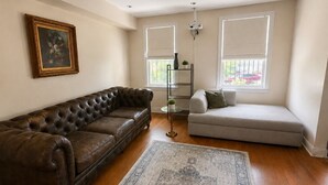 Een woonkamer met een bruine leren bank, een lichtkleurige slaapbank, een kamerbreed tapijt en een schilderij aan de muur.