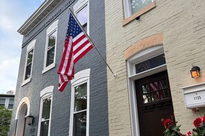 Ein zweistöckiges Gebäude mit einer Fahnenstange, an der eine amerikanische Flagge weht, einem Briefkasten mit der Nummer 1135 und einer Tür mit einem Fenster.
