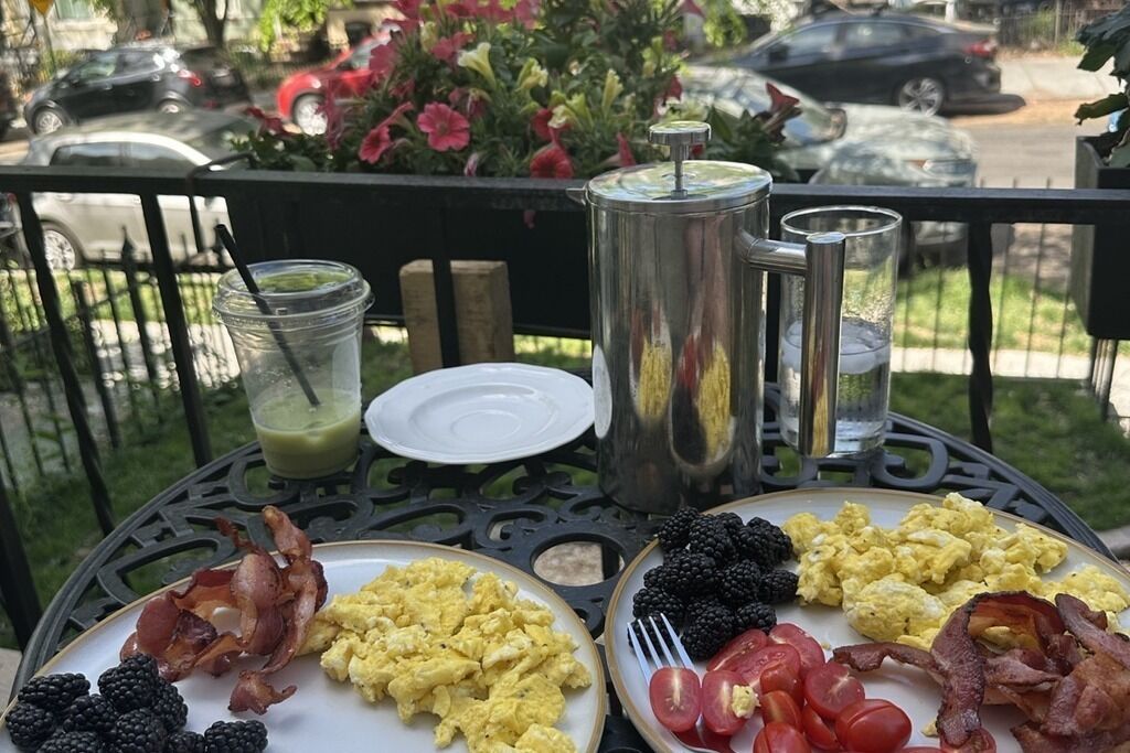 Ett bord med frukosträtter, inklusive äggröra, bacon, tomater, hallon och en grön smoothie.