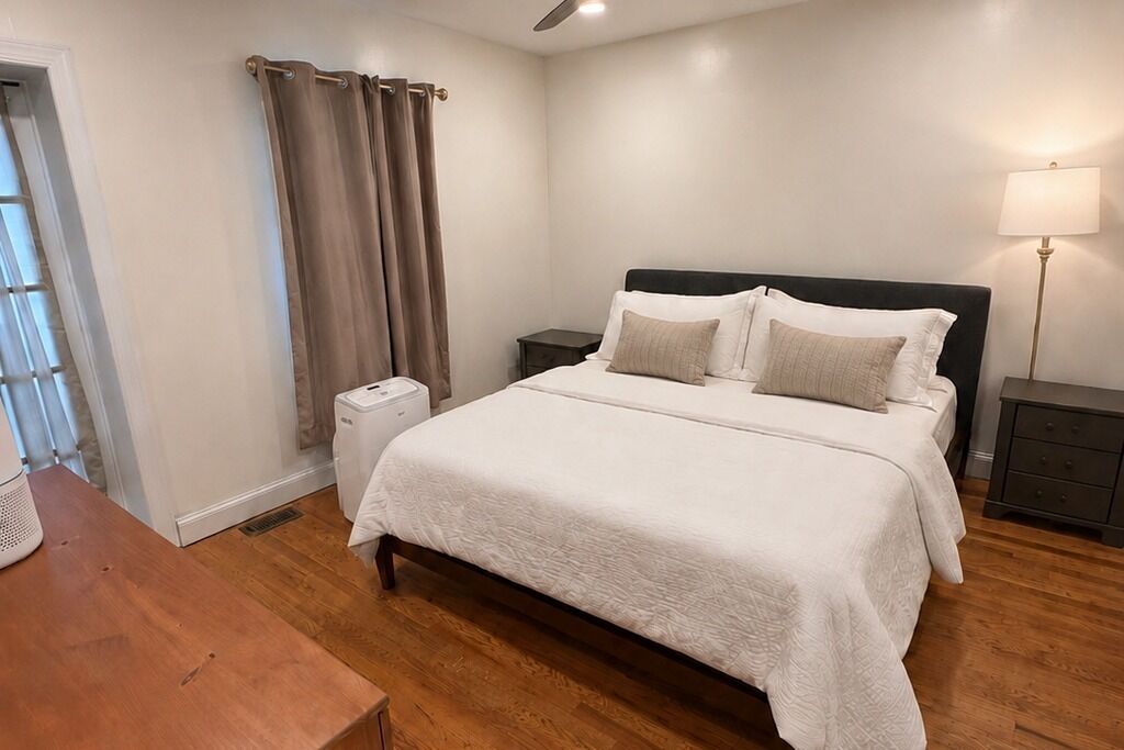 Une chambre à coucher avec un lit, des tables de chevet, une lampe et une fenêtre avec des rideaux.