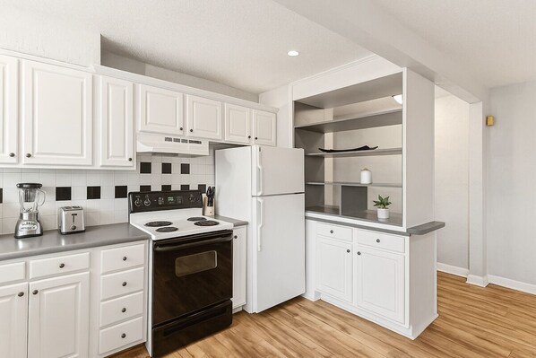 Une cuisine moderne avec des meubles blancs, une cuisinière noire, un réfrigérateur et un four encastré.