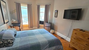 A bedroom with a bed, wooden dresser, TV, and a window with curtains. - Kevinsrentals Dot Com (Providence)