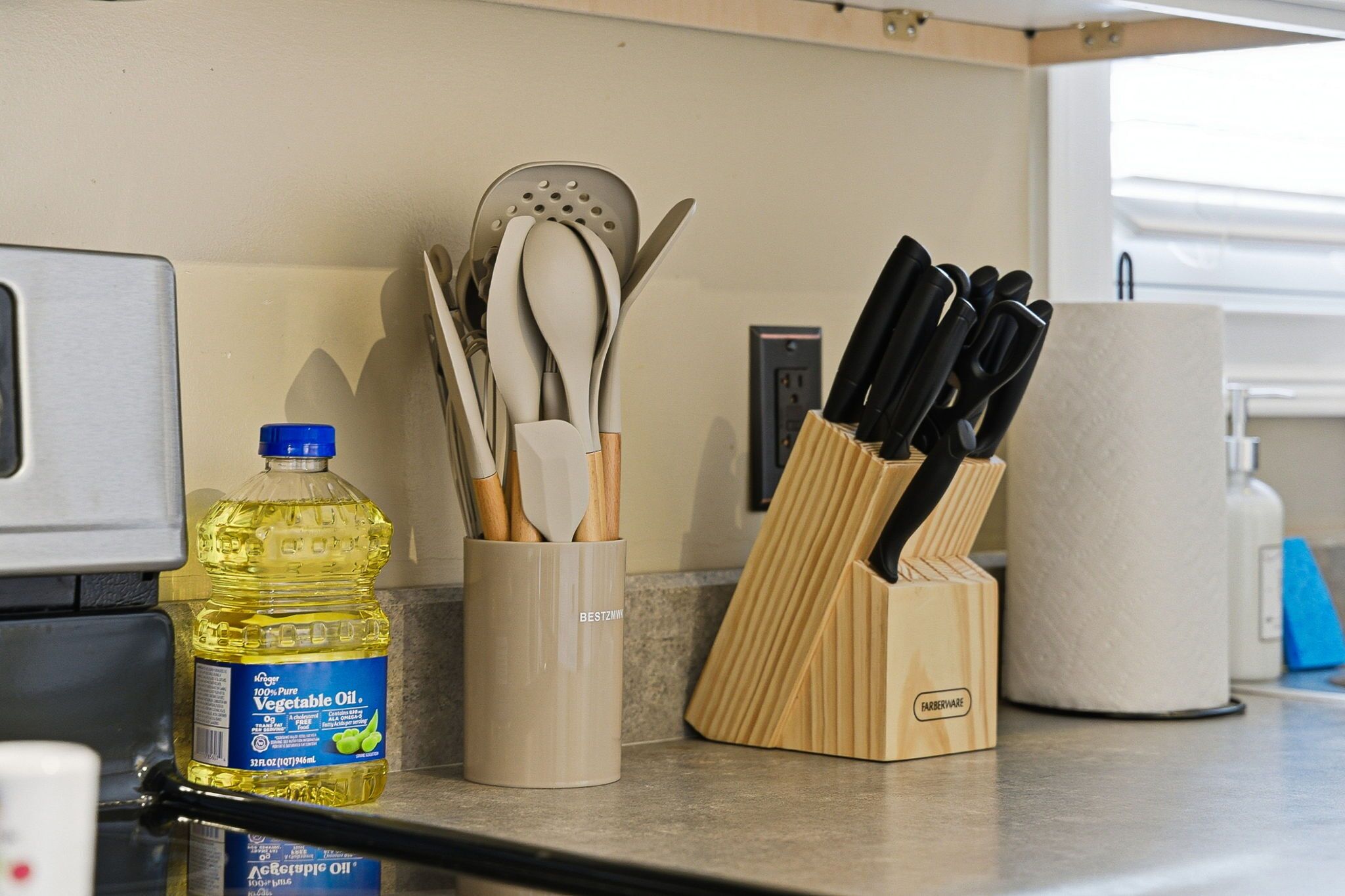 A kitchen counter with a bottle of vegetable oil, a utensil holder, and a knife block.