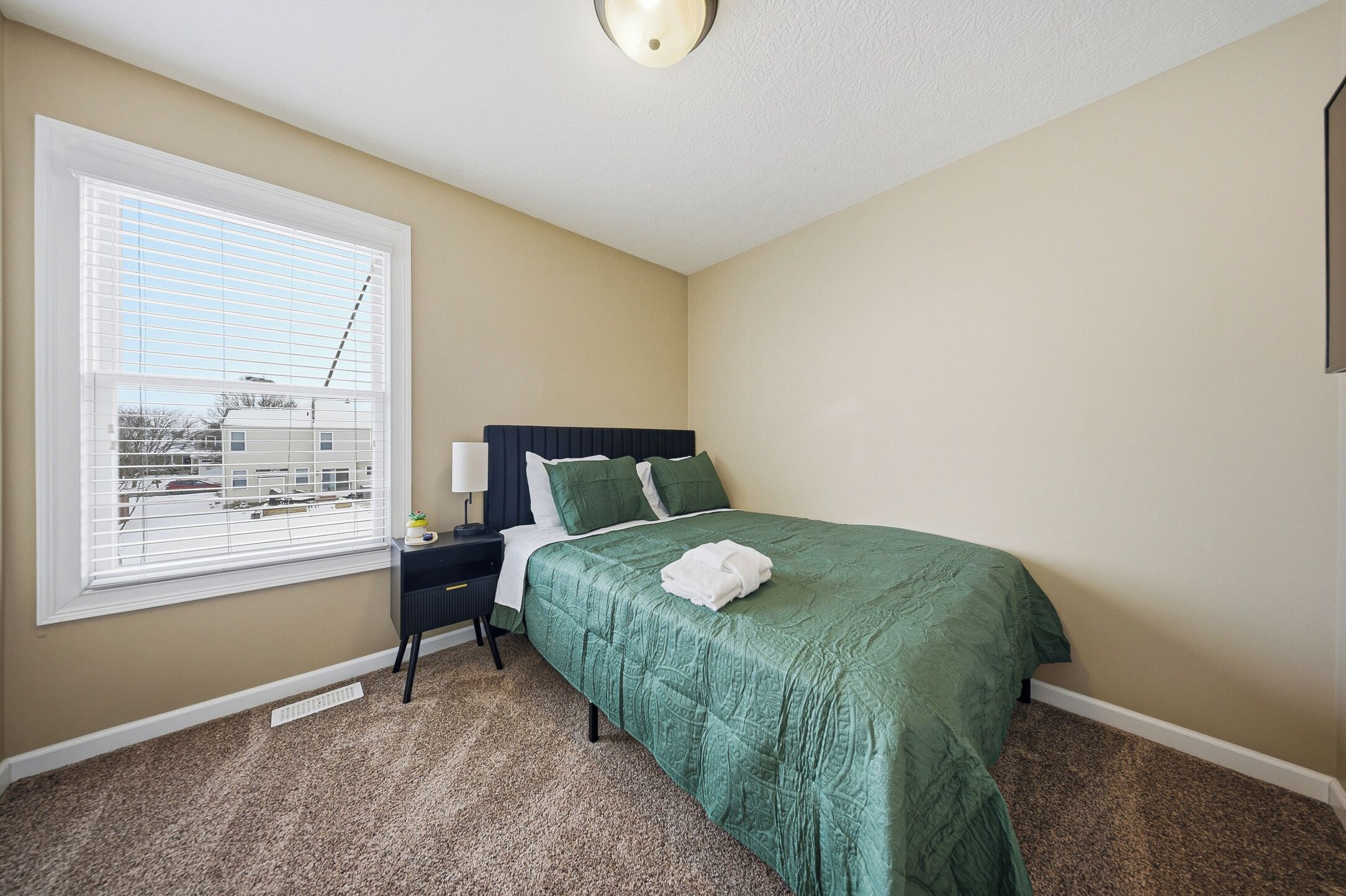 A bedroom with a bed, a nightstand, a window with blinds, and a ceiling light.