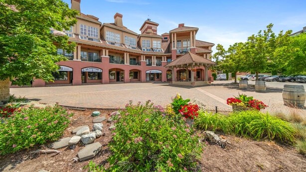 A large, multi-story building with a central courtyard, surrounded by lush greenery and flower beds. - Family Studio - 202B (Kelowna)