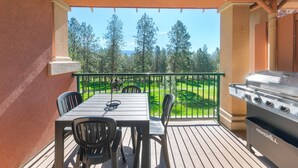 A balcony with a table and chairs, a grill, and a view of trees and a golf course. - Family Studio - 202B (Kelowna)