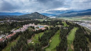 A golf course with a lake, surrounded by residential buildings and a mountainous backdrop.