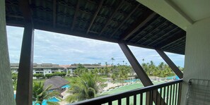 A view from a balcony with a pool, palm trees, and resort buildings in the background. - Beach Class Muro Alto Resort (Ipojuca)