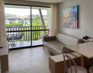 Een moderne woonkamer met een bank, een eettafel en stoelen. Er is een balkon met uitzicht op gebouwen en groen.