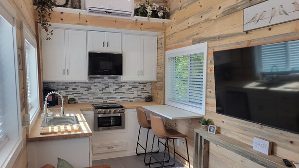 A compact kitchen with white cabinets, a built-in stove, and a large window with blinds. - Tiny home in Van Alstyne with easy access to Hwy 75 and exceptional privacy. (Van Alstyne)