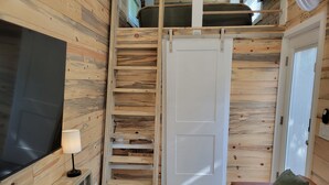 A cozy room with a TV, a lamp, a couch, and a sliding door. - Tiny home in Van Alstyne with easy access to Hwy 75 and exceptional privacy. (Van Alstyne)