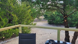 A deck with a chair and a table, surrounded by trees and a gravel path. - Tiny home in Van Alstyne with easy access to Hwy 75 and exceptional privacy. (Van Alstyne)