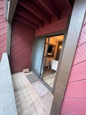 Eine Holzterrasse mit einer Schiebetür, die zu einem Innenraum führt.