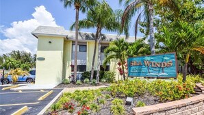 A building with a sign reading "SEA WNDs" surrounded by tropical plants and palm trees.