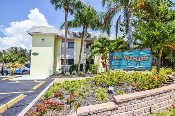 A building with a sign reading "SEA WNDs" surrounded by tropical plants and palm trees.
