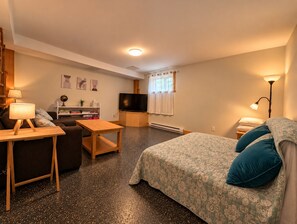 A cozy room with a bed, a desk, a television, and a bookshelf. - Full Guest Suite (Wakefield)