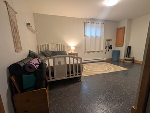 Une pièce comprenant un lit, un berceau, un tapis de yoga, une petite table avec une lampe, une fenêtre avec des rideaux et un porte-bagages fixé au mur.