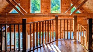Interior de madera con techo inclinado, ventilador de techo y ventanas amplias que dan a vistas de vegetación.