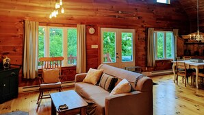 A cozy cabin interior with a wooden ceiling, a sofa, a dining table, and large windows offering a view of greenery. - Private Escape For 2 (Wakefield)