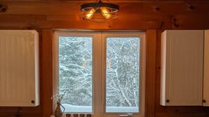 A kitchen with wooden cabinets, a double sink, and a window with a view of snow-covered trees. - Private Escape For 2 (Wakefield)