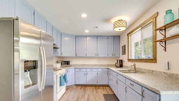 Una cocina con armarios azul claro, un refrigerador de acero inoxidable, un microondas y un lavamanos.