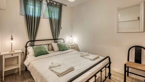 Ein ordentlich bezogenes Bett mit weißen Leinen und grünen Kissen, eine Nachttischlampe, ein Stuhl und ein Spiegel an der Wand.