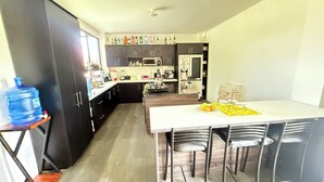 A modern kitchen with dark cabinets, a white countertop, and a dining area with a table and chairs. - Villa Mariaclaudia Macas (Macas)