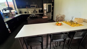 A modern kitchen with dark cabinets, a white countertop, and a central island with chairs. - Villa Mariaclaudia Macas (Macas)