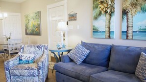 A living room with a blue sofa, a patterned armchair, and a small round table with a lamp. - Compass Bayfront Condo, Close to Beach & Pool! (Corpus Christi)