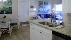 A kitchen with white cabinets, a granite countertop, a sink, and a ceiling fan. - Compass Bayfront Condo, Close to Beach & Pool! (Corpus Christi)