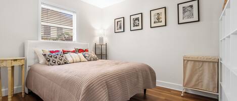 Ein Schlafzimmer mit Bett, Nachttisch, Lampe und Deckenventilator. An der Wand hängen vier gerahmte Bilder.