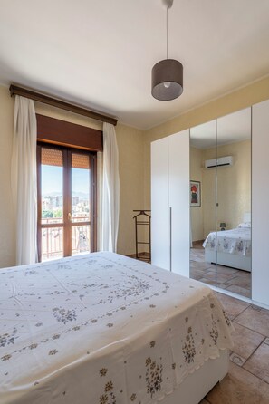 Ein Schlafzimmer mit einem Bett, einem Kleiderschrank, einer Hängeleuchte und Blick durch ein Fenster.