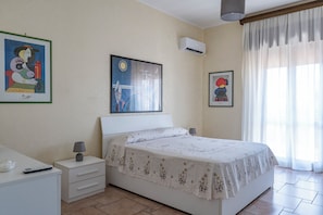 A bedroom with a bed, a nightstand, a lamp, a wall-mounted air conditioner, and two framed artworks. - At Mom's (Palermo)