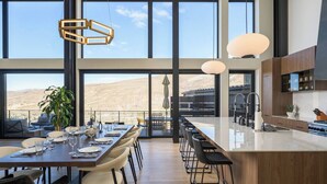 A modern kitchen with a large island, a dining area with a view of the mountains, and large windows. - Whiskey Hill Luxury Retreat | Hot tub + Mountain Views (Vail)